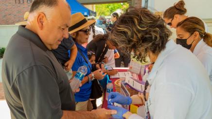 Assemblymember Rodriguez getting his finger poked with a needle at the Summer Open House & BBQ
